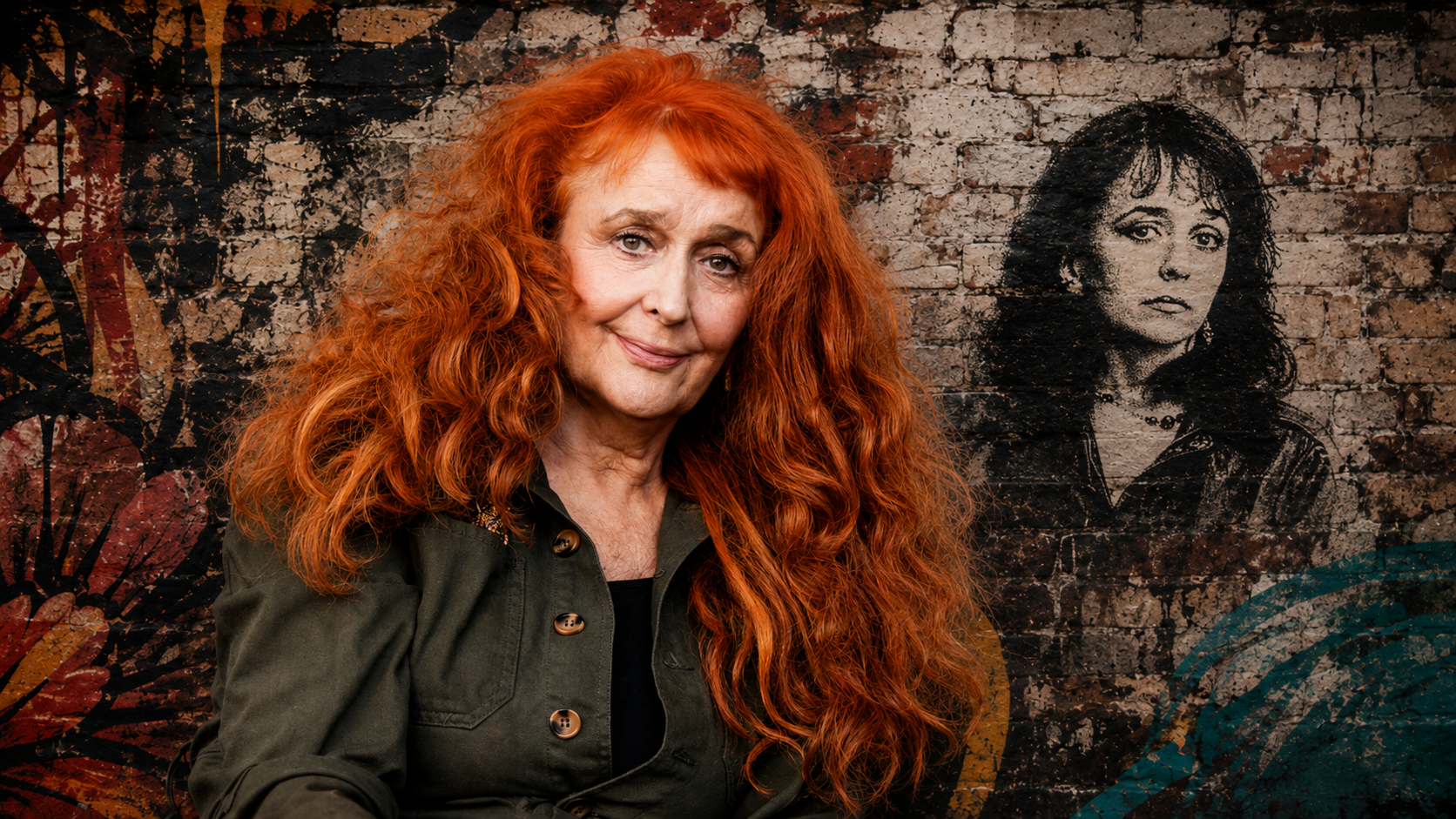 Kay Adshead seated before a painted brick wall bearing a mural portrait.
